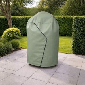 Clarijs BBQ hoes in de kleur mat olive over een kamado barbecue van The Bastard in een tuinsetting. Duurzame PVC beschermhoes die je barbecue beschermt tegen regen en vuil.
